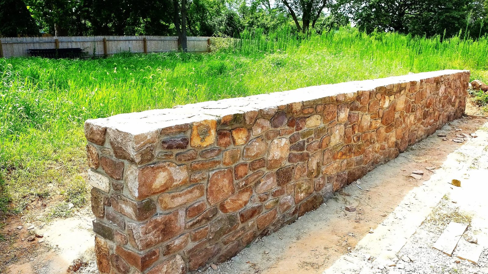 Fieldstone retaining wall with a flat cap through a meadow